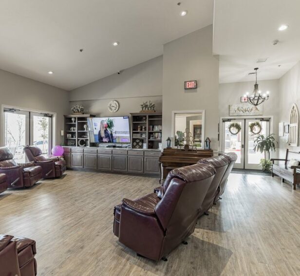Spacious assisted living community lounge with comfortable recliner chairs, a television, and bright natural light creating a welcoming environment for senior residents.
