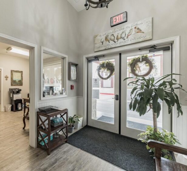 Welcoming assisted living community entrance with glass doors, seasonal wreaths, and a clean, well-lit interior hallway.