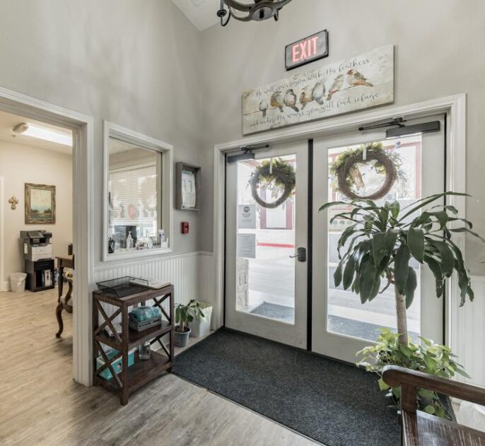 Welcoming assisted living community entrance with glass doors, seasonal wreaths, and a clean, well-lit interior hallway.