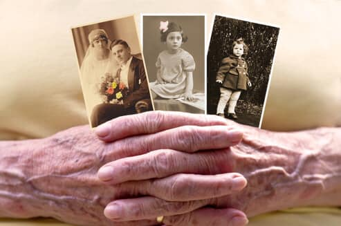 Elderly hands clasped with three vintage family photographs.